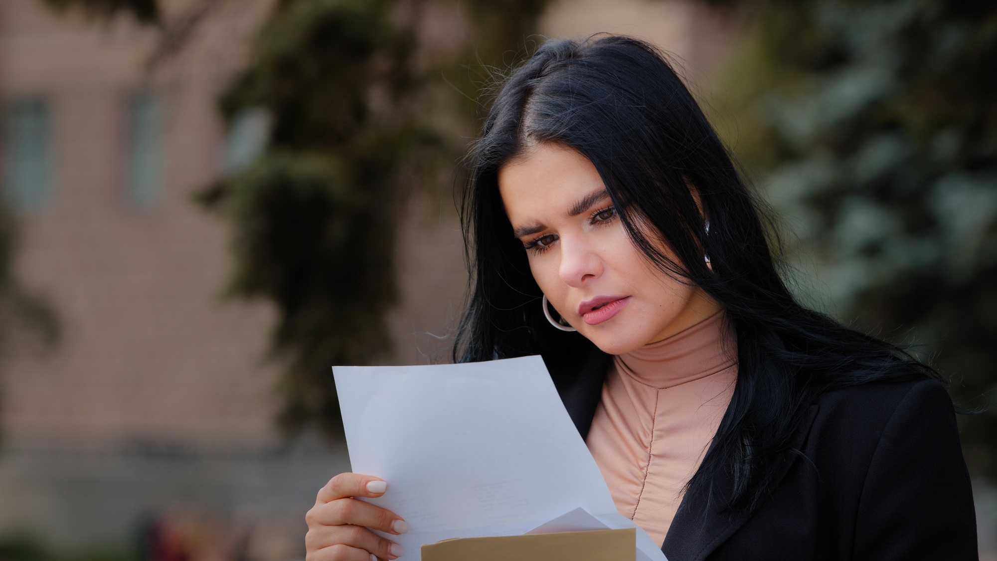 Close-up serious young woman sitting outdoors reading paper letter sad girl feels resentment upset