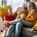 Happy adult couple at home doing video call with friends sitting on the sofa during morning