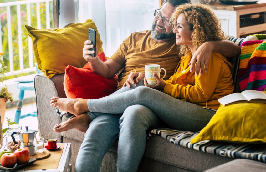 Happy adult couple at home doing video call with friends sitting on the sofa during morning