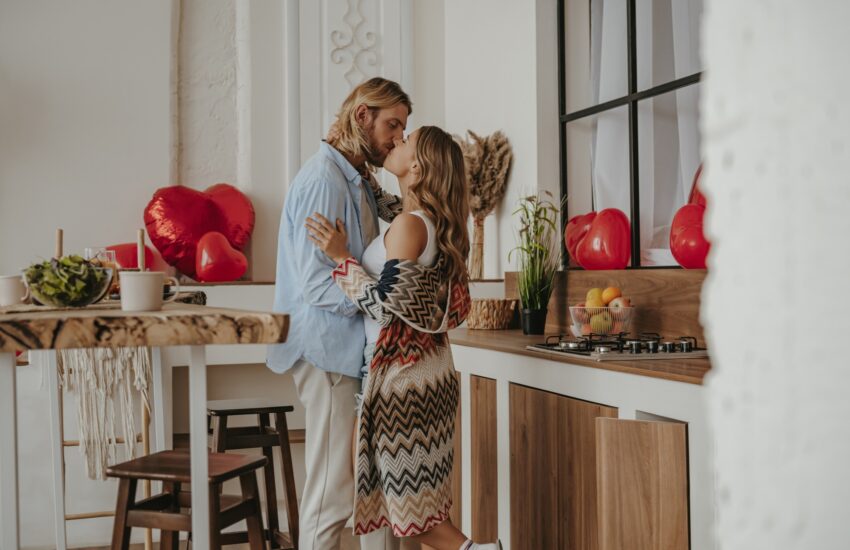 Romantic young couple embracing and kissing while celebrating love anniversary at the decorated home
