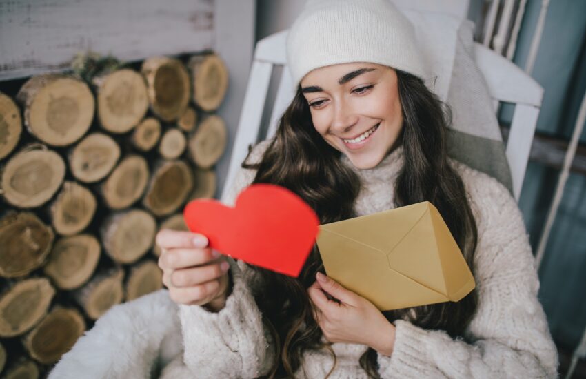 Young beautiful woman opening letter with Valentine’s Day holiday greeting card heart shaped.