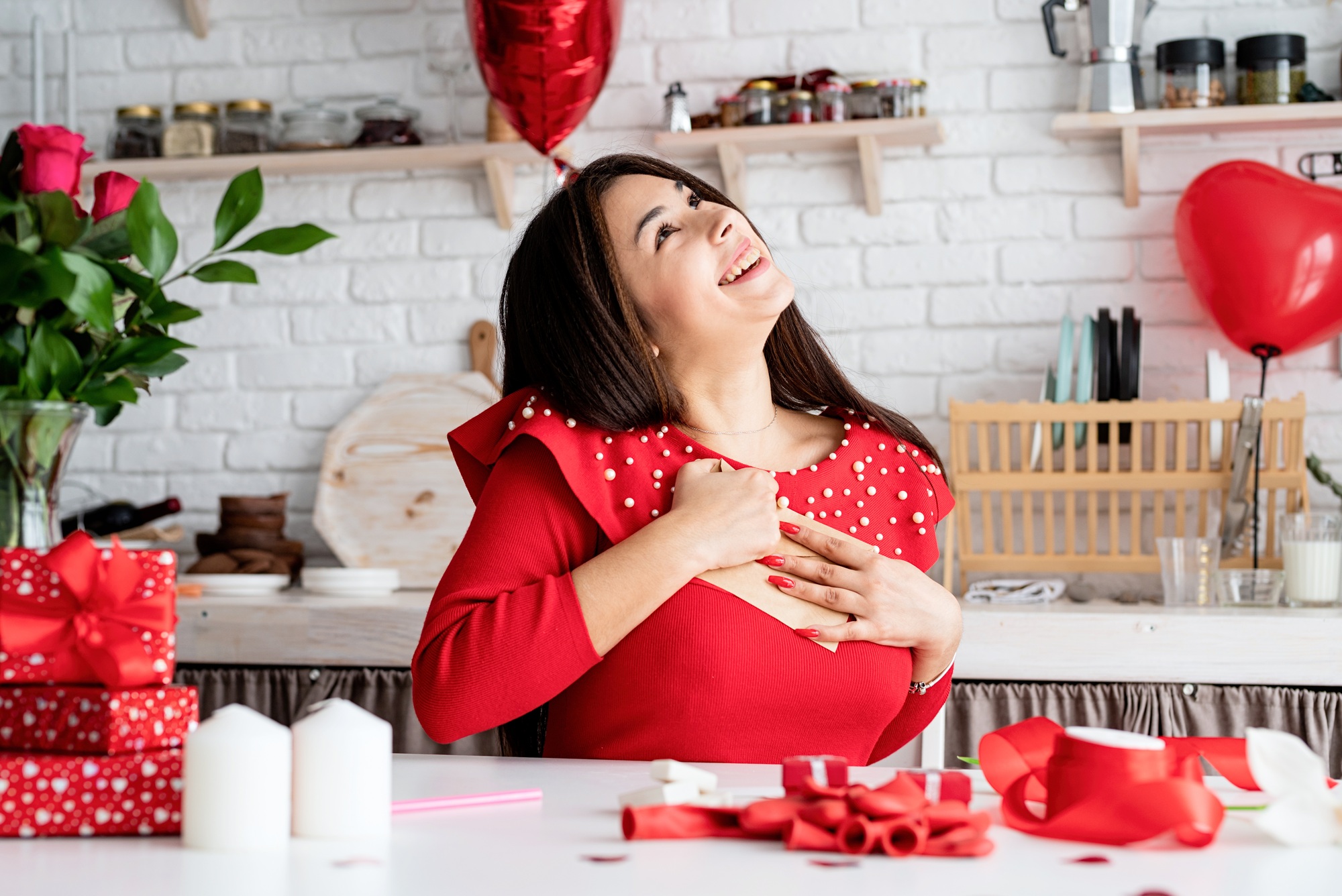 Young romantic woman in red dress writing love letter sitting at the decorated kitchen